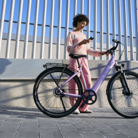sfeerbeeld met mevrouw op de telefoon die een roze tenways fiets vasthoudt op de straat ebike gelderland