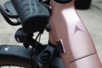 Detail van het roze frame met merkembleem, naast de koplamp en voorvork.